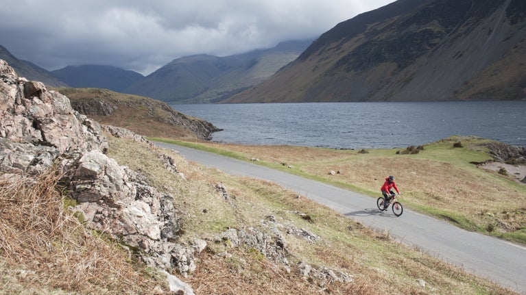 Cyclist riding their bike on the road alongside Wastwater with mountain views in the background